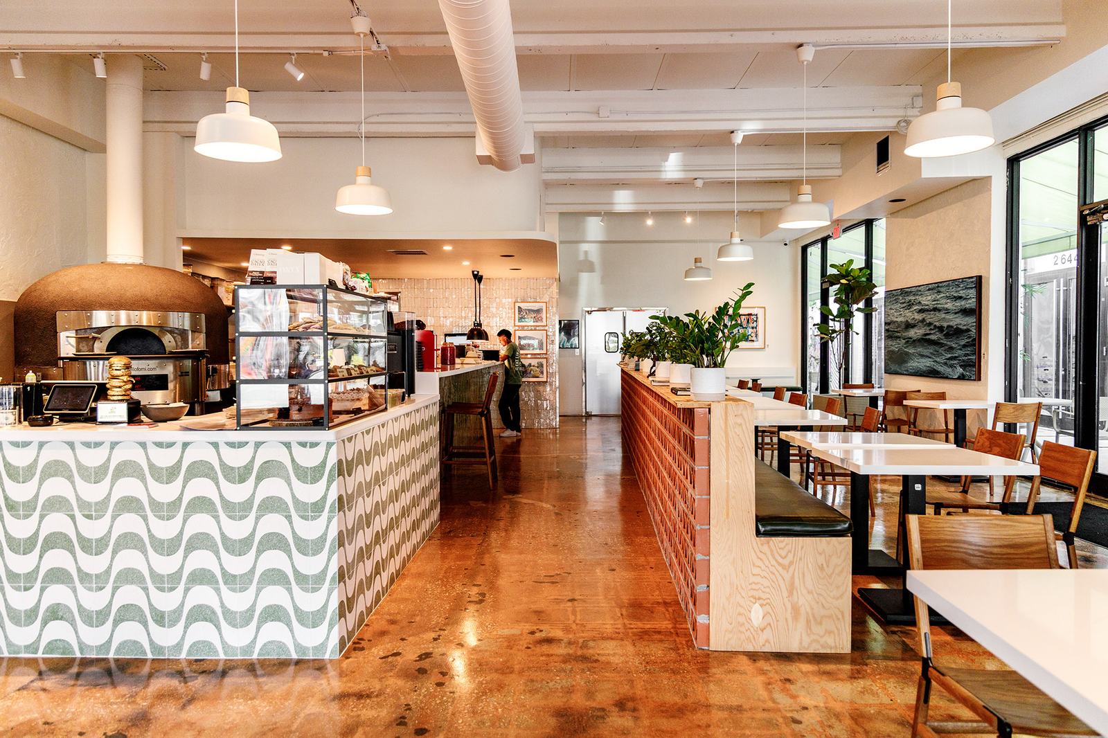 The bright Love Life Cafe dining room with long communal tables, a pizza oven and a wavy tiled counter.