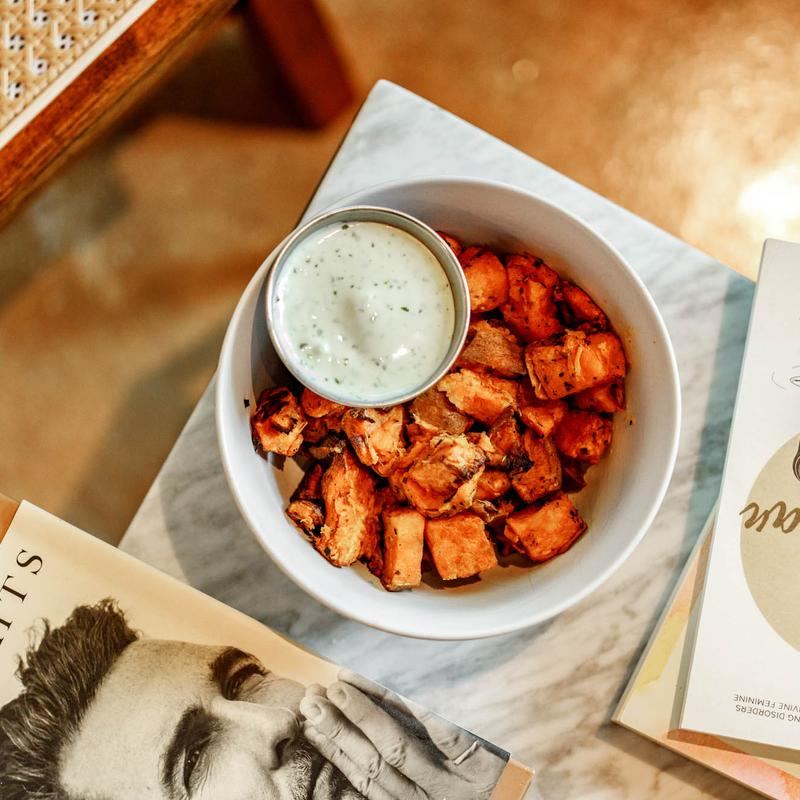 A bowl of roasted sweet potatoes with a creamy herb dip.