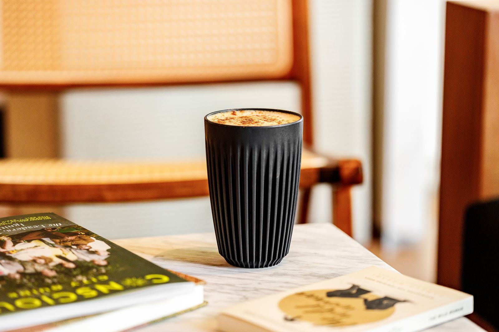 A black cup of coffee on a marble table beside a chair.