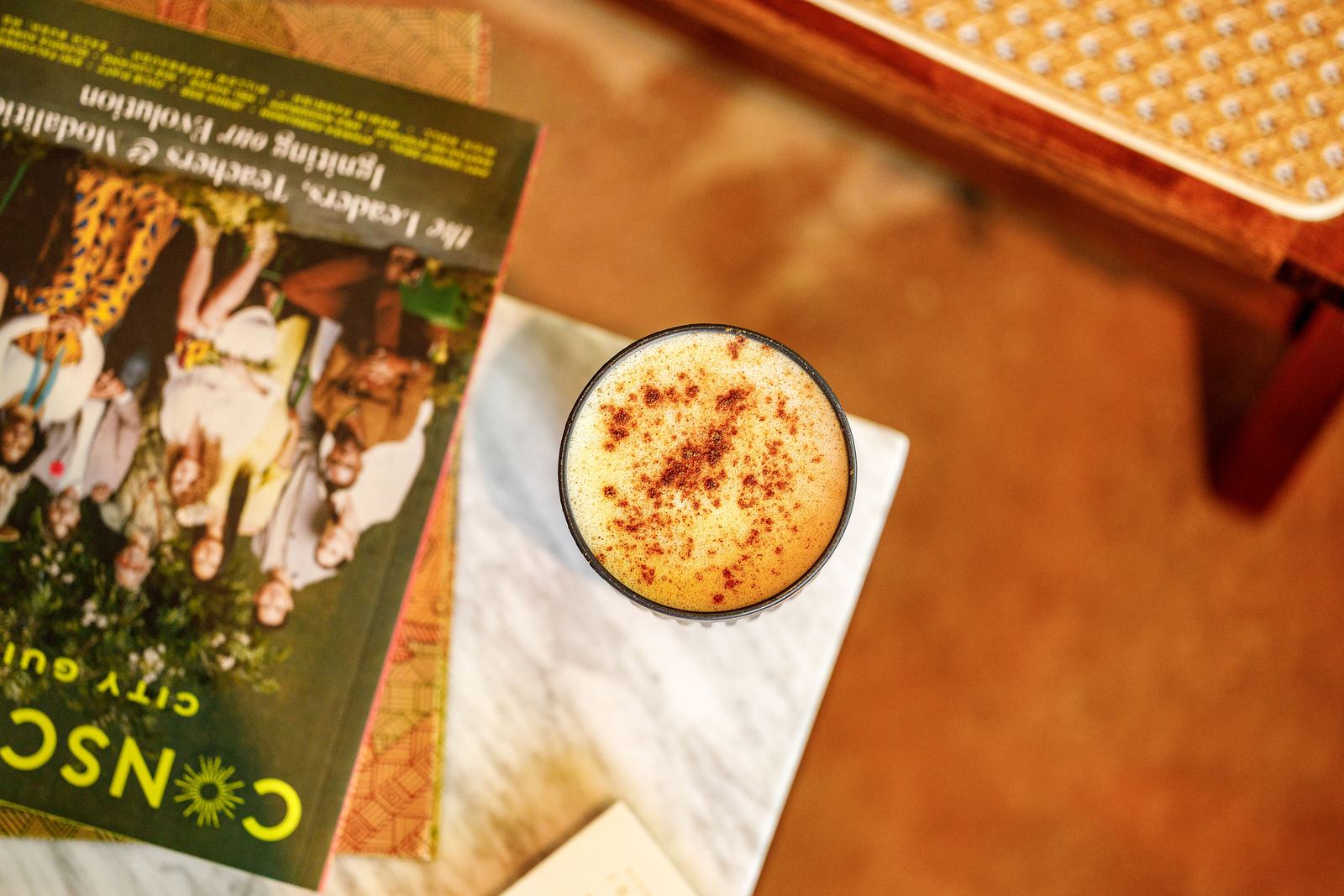 A golden latte in a small cup on a marble tray beside a book.